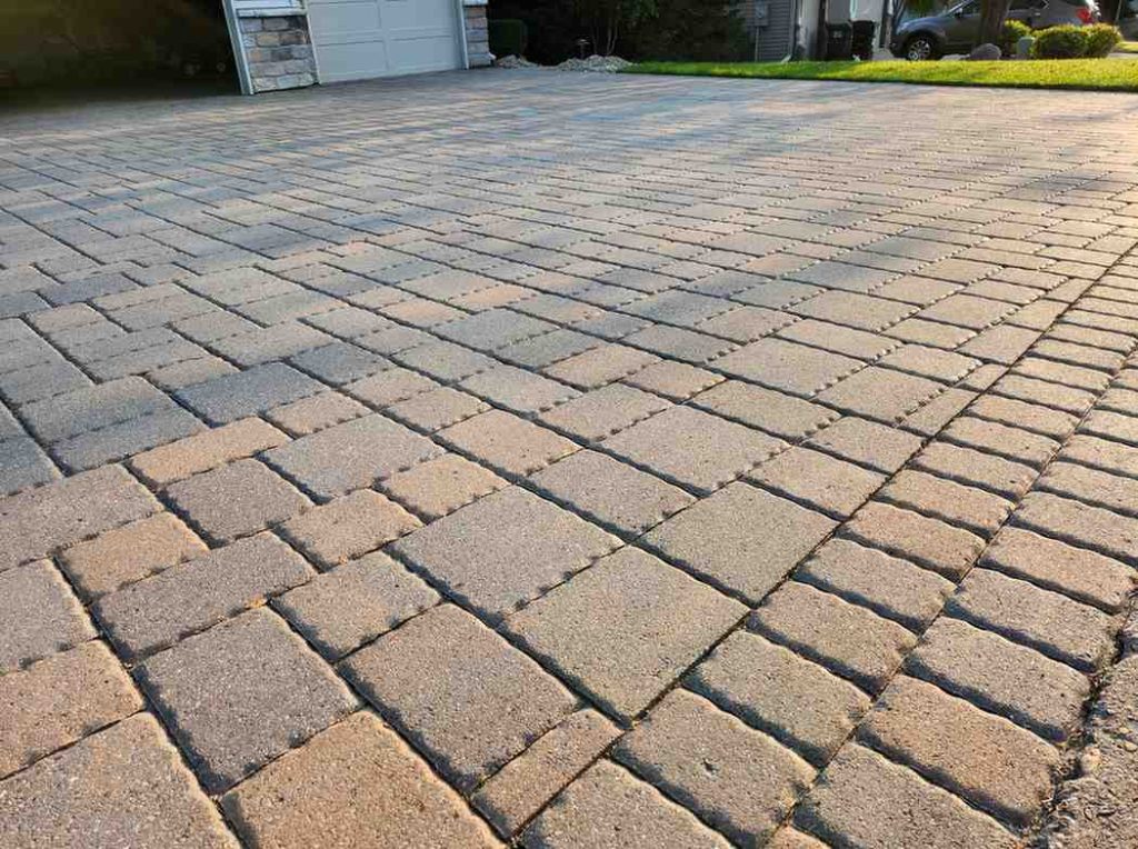 Interlocking concrete paver driveway extending toward a two-car garage with a green lawn visible at the edge