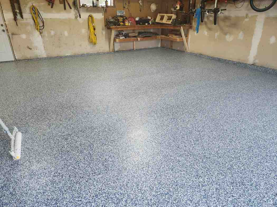 Clean, speckled gray epoxy garage floor in a cluttered workshop with tools on the walls and a workbench at the back edge of the room.